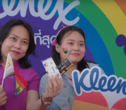 Image shows two people posing at a Thai Pride event in front of the Kleenex brand logo, both have rainbow stickers on their cheeks.