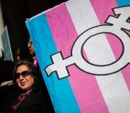 An activist holds up a trans Pride flag with the transgender chevron printed on top of it.
