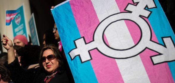 An activist holds up a trans Pride flag with the transgender chevron printed on top of it.