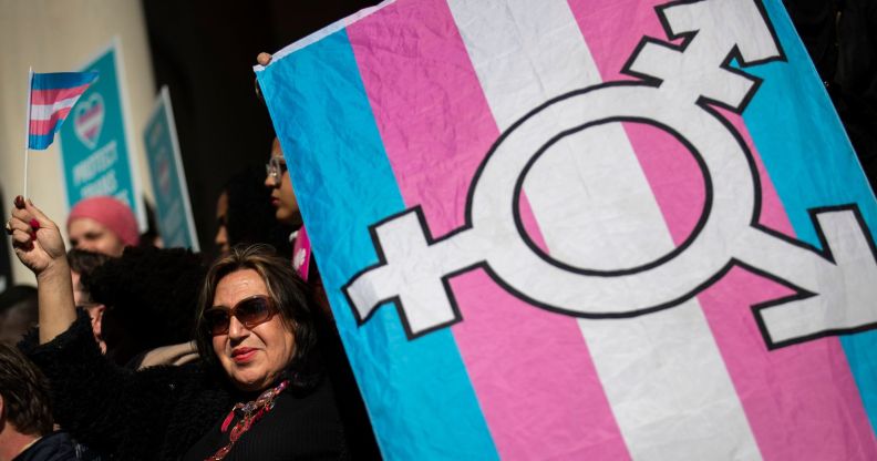 An activist holds up a trans Pride flag with the transgender chevron printed on top of it.
