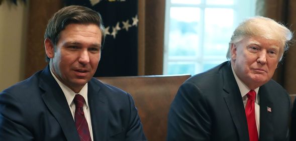 Republican politicians Ron DeSantis and Donald Trump sit side by side in the White House
