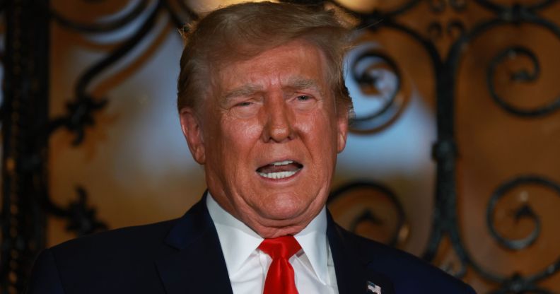 Former president Donald Trump wears a suit and tie and he appears before a door