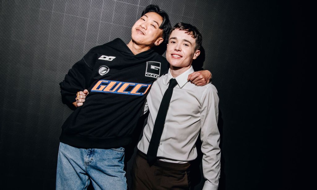 Jes Tom, a comedian featured on Hannah Gadsby's Netflix special Gender Agenda, wears a sweatshirt and jeans while hugging trans actor Elliot Page with one arm