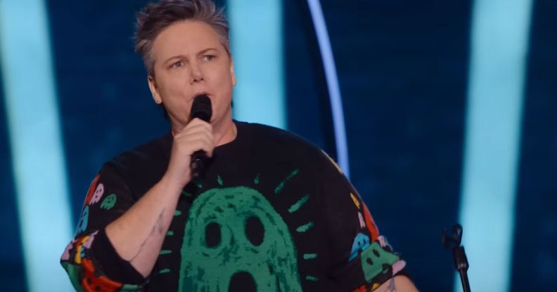 Australian comedian Hannah Gadsby wears a black shirt with a green ghost on it while speaking into a microphone during their new trans-led Netflix special Gender Agenda