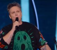 Australian comedian Hannah Gadsby wears a black shirt with a green ghost on it while speaking into a microphone during their new trans-led Netflix special Gender Agenda