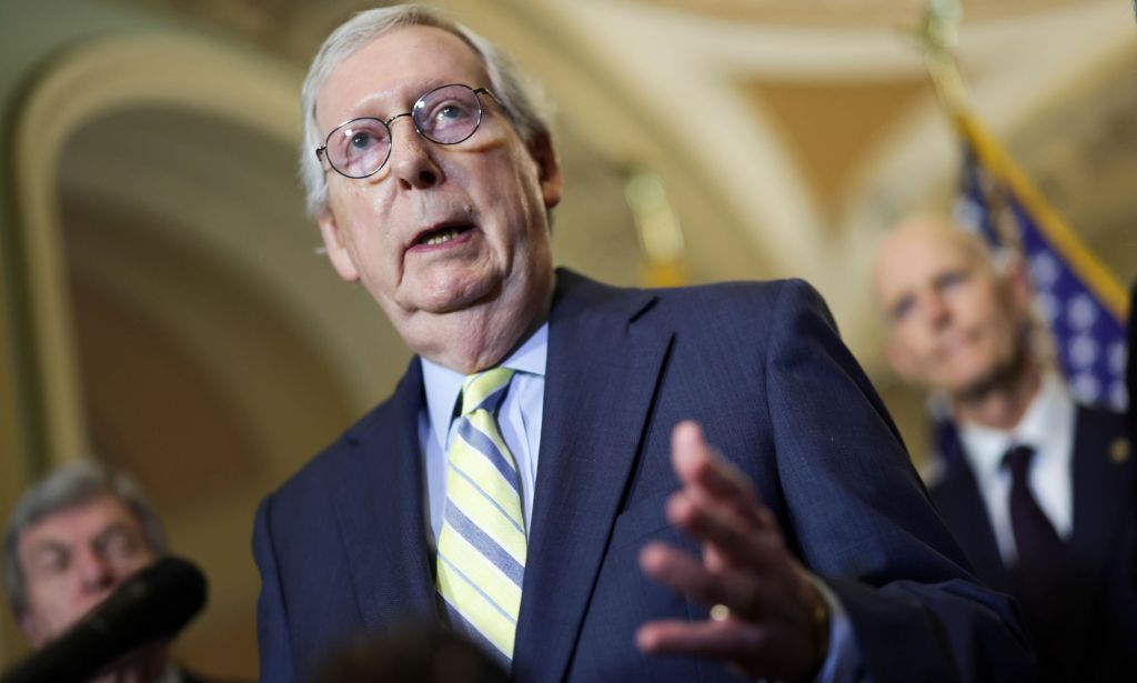 Senator Mitch McConnell wears a suit and tie as he speaks at a podium to people off screen