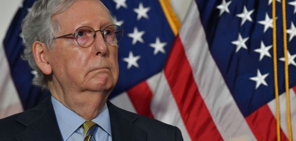 Senate Republican leader Mitch McConnell wears a suit and tie as he stands in from a red, white and blue US flag