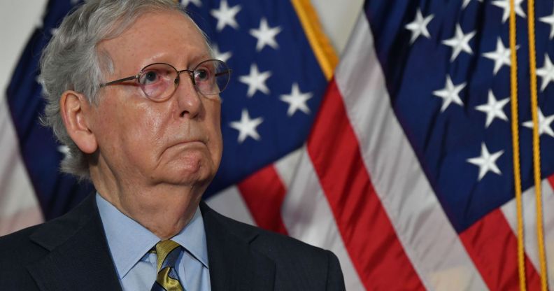 Senate Republican leader Mitch McConnell wears a suit and tie as he stands in from a red, white and blue US flag