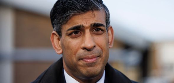 Prime minister Rishi Sunak wears a suit, tie and coat as he stands outside for a photo