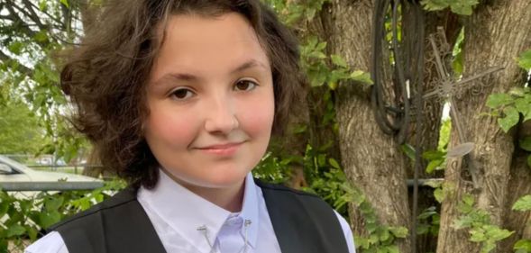 Oklahoma non-binary teen Nex Benedict, who died on 8 February 2024, wears a light coloured shirt and dark vest as they stand outside