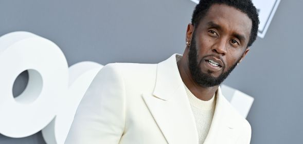 Music mogul Sean "Diddy" Combs wears a white shirt and matching suit while posing for a picture at an event