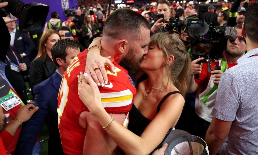 Singer Taylor Swift wears a black outfit as she kisses her boyfriend Travis Kelcee, who is wears a red and yellow Kansas City Chiefs jersey, during the 2024 Super Bowl
