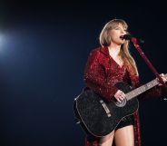 Taylor Swift wears a red sparkly outfit as she holds a guitar and sings into a microphone during a performance