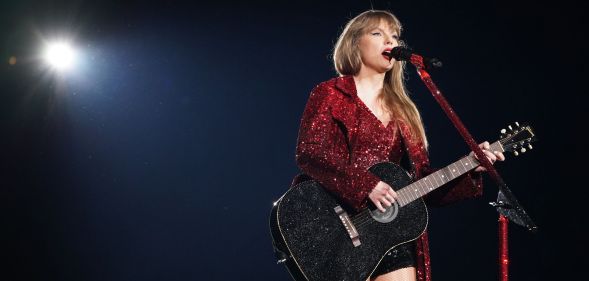 Taylor Swift wears a red sparkly outfit as she holds a guitar and sings into a microphone during a performance