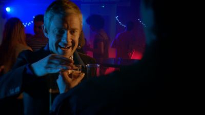 Scene from BBC TV show Sherlock featuring Martin Freeman in a dimly lit club, the lights are blue and purple