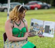 Image shows drag queen Aime Vanite reading a childrens book outdoors
