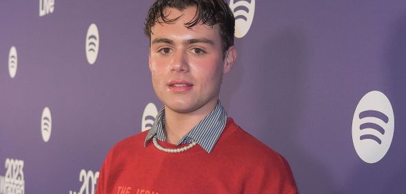 Heartstopper star Bradley Riches wears a red jumper with gelled hair