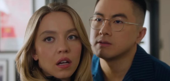 Sydney Sweeney (blonde, long hair) poses with Asian, glasses wearing comedian Bowen Yang, who has short dark hair, in an SNL skit