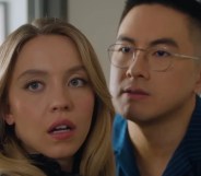 Sydney Sweeney (blonde, long hair) poses with Asian, glasses wearing comedian Bowen Yang, who has short dark hair, in an SNL skit