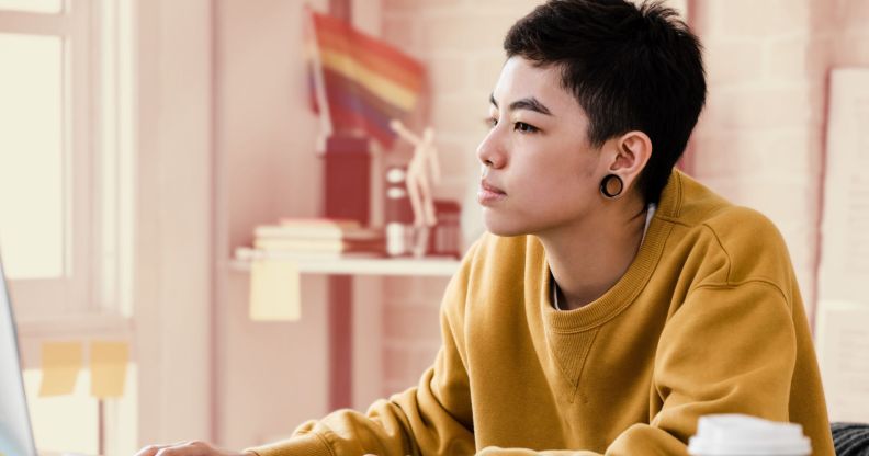 This is an image of a person working at a computer. They present genderqueer. They have large gauge earrings and are wearing a yellow jumper.