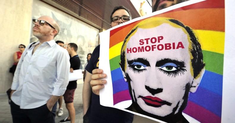 TOPSHOT - A demonstrator holds a poster depicting Russian President Vladimir Putin with make-up as he protests against homophobia and repression against gays in Russia, in front of the Russian Embassy in Madrid on August 23, 2013. AFP PHOTO/ GERARD JULIEN (Photo by GERARD JULIEN / AFP) (Photo by GERARD JULIEN/AFP via Getty Images)