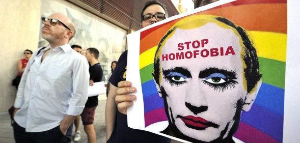 TOPSHOT - A demonstrator holds a poster depicting Russian President Vladimir Putin with make-up as he protests against homophobia and repression against gays in Russia, in front of the Russian Embassy in Madrid on August 23, 2013. AFP PHOTO/ GERARD JULIEN (Photo by GERARD JULIEN / AFP) (Photo by GERARD JULIEN/AFP via Getty Images)