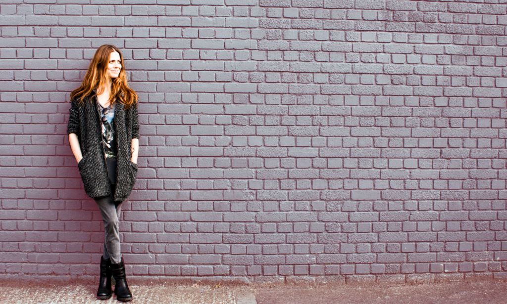 This is a picture of a woman leaning on a wall. She has red hair and is wearing black