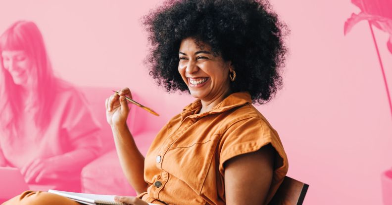 This is an image of a Black woman wearing an orange jumpsuit. She is in a work meeting and is smiling. She is above a pink backgroud.
