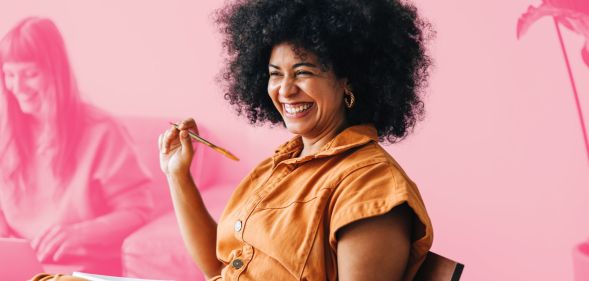 This is an image of a Black woman wearing an orange jumpsuit. She is in a work meeting and is smiling. She is above a pink backgroud.