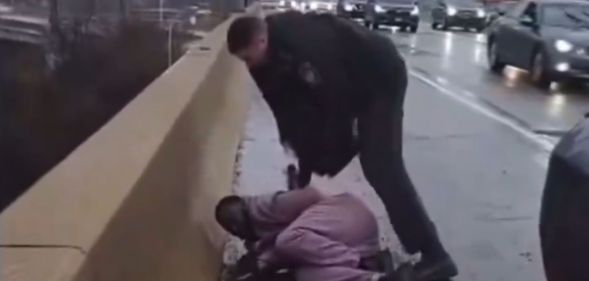 A police officer stands over a man lying on the floor on the side of the road.