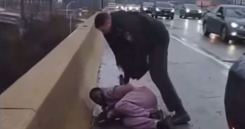 A police officer stands over a man lying on the floor on the side of the road.