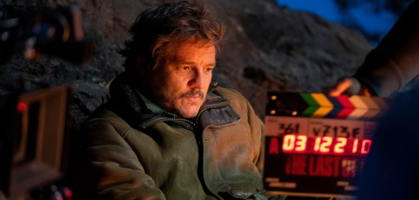 Pedro Pascal sat in a cowboy jacket with a filmling clapper board in front of him.