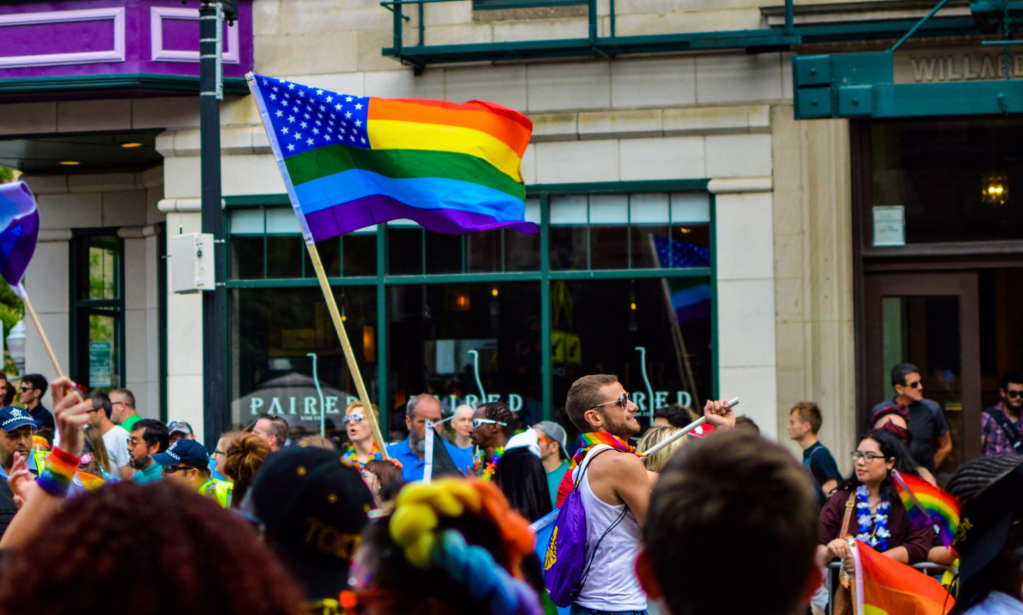 A Pride flag stylised like the US flag being waved at a Pride parade (Canva)