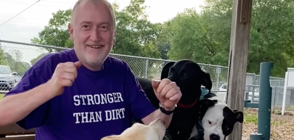 John Walter Lay who was fatally shot at West Dog Park in Tampa, he is wearing a purple shirt that reads 'stronger than dirt' and is surrounded by three dogs.