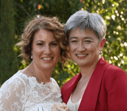 Photo shows Penny Wong on the right in a red suit, and her partner Sophie on the left in a wedding dress, smiling in a garden