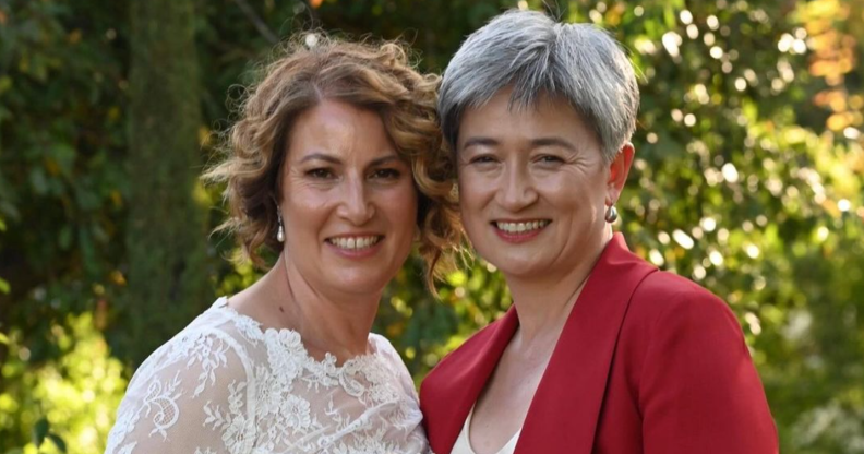 Photo shows Penny Wong on the right in a red suit, and her partner Sophie on the left in a wedding dress, smiling in a garden