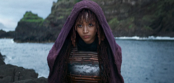 Amandla Stenberg in The Acolyte, standing on the seashore wearing a purple hooded robe