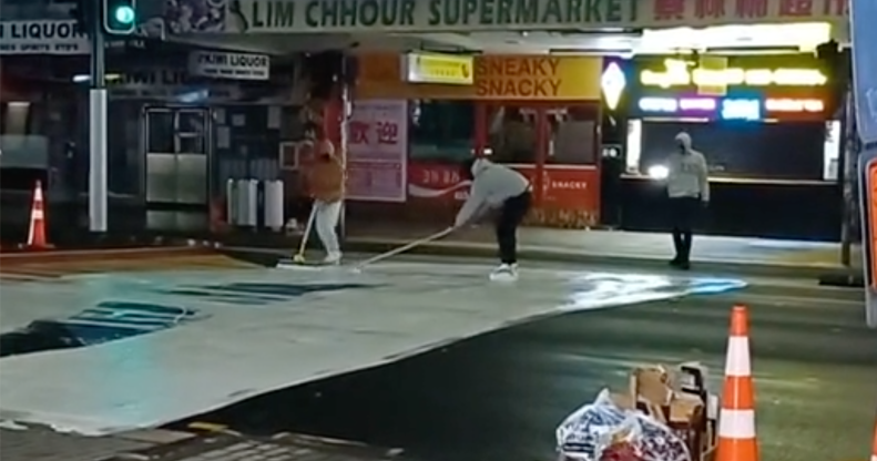 A video shows three people painting over a rainbow, Pride-themed crossing in Auckland