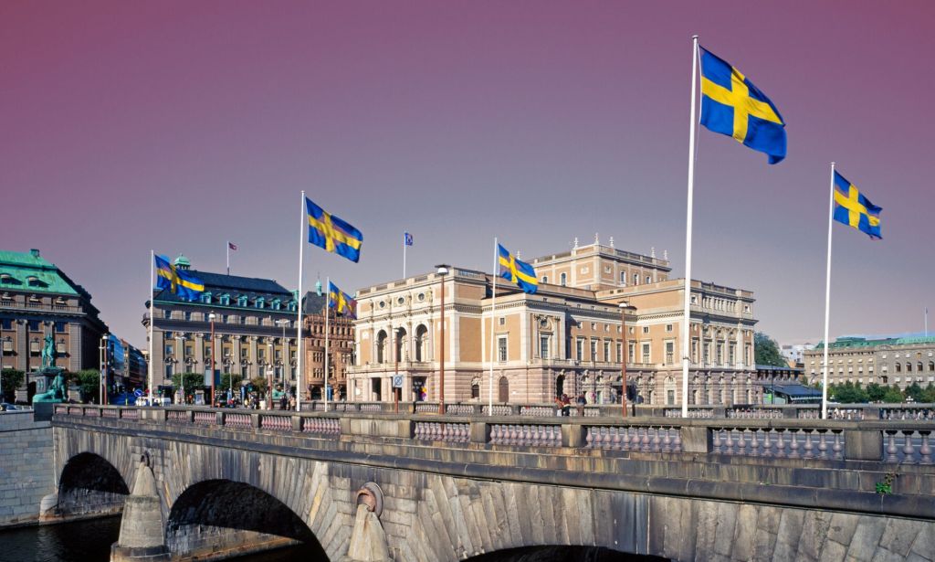 This is an image of multiple Swedish flags flying around what resembles a castle. 