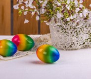three rainbow easter eggs on a white table beside a white knitted pot with purple flowers