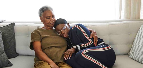 Stock image illustrating cancer shows woman wearing headscarf hugging her mother on the sofa