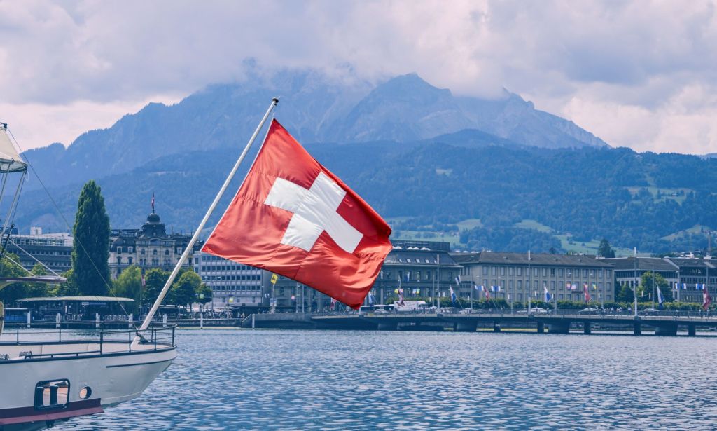 This is an image of the Swiss flag on the back of a boat. In the background there is a mountain.