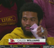 Caleb Williams seen wearing a yellow hoodie and holding a pink phone case at a basketball game