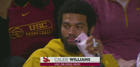Caleb Williams seen wearing a yellow hoodie and holding a pink phone case at a basketball game