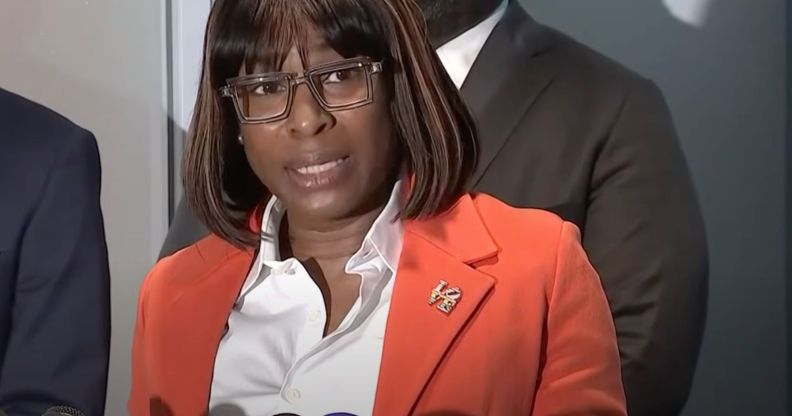 Philadelphia LGBTQ+ official Celena Morrison wears a white shirt and orange-red jacket as she speaks into microphones during a press conference