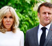 French president Emmanuel Macron wears a suit and tie as he stands beside his wife Brigitte, who is wearing white