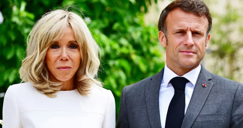 French president Emmanuel Macron wears a suit and tie as he stands beside his wife Brigitte, who is wearing white