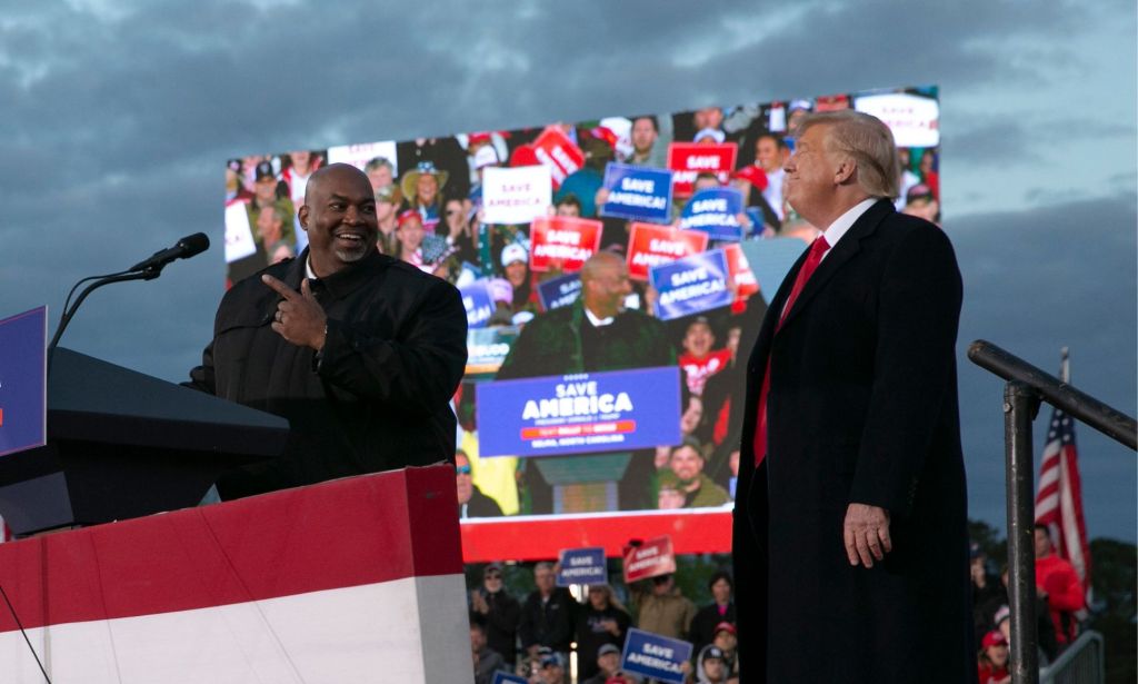 North Carolina lieutenant governor Mark Robinson smiles while standing at a podium and looking towards former president Donald Trump