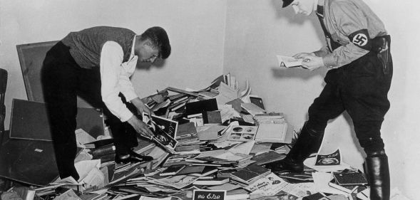 Nazi demonstrators stand above a pile of books, papers and research about the trans community during WWII