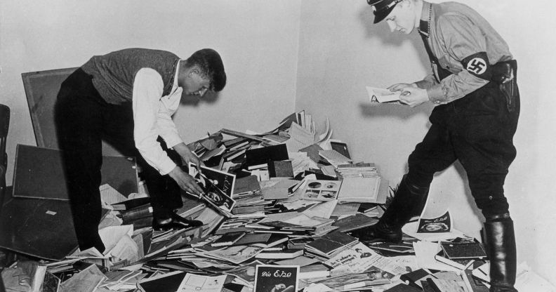 Nazi demonstrators stand above a pile of books, papers and research about the trans community during WWII